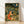 Whimsical cottagecore poster art depicting a fox wearing a hat seated among blooming flowers and lush plants beneath a glowing moon, rendered in warm oranges, deep teals, and soft creams.