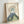 Framed poster art depicting Mount Fuji under a radiant sunrise in traditional woodblock style, with minimal composition using soft sage, slate, cream, and rust earth tones.