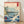 Serene Japanese woodblock print featuring a sailboat navigating deep blue waters beneath majestic mountains, with pine trees and birds in cream, teal green, and red tones.