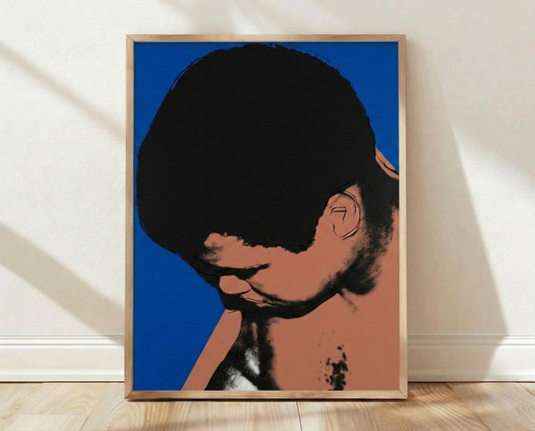 Pop art portrait of Muhammad Ali in vibrant colors with bold graphic layering, framed poster on wall.