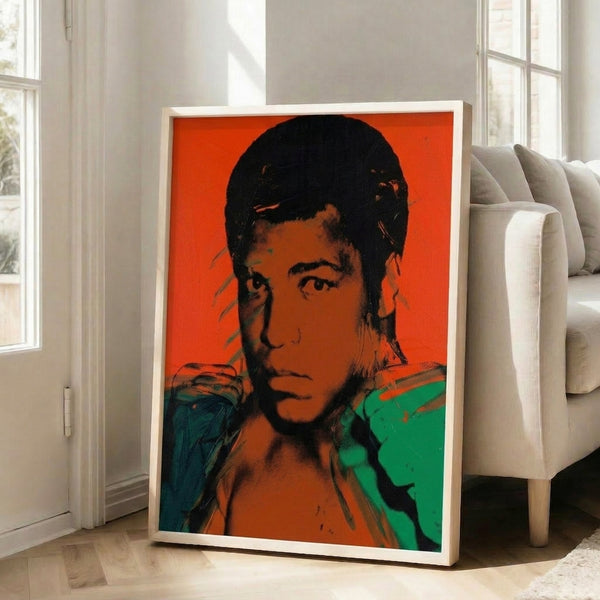 Warhol-inspired pop art poster of Muhammad Ali with layered color fields and high-contrast technique in a frame on white wall.