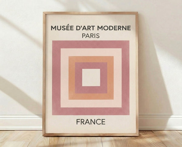 Bauhaus geometric poster with overlapping squares in mauve, dusty pink, peach, and cream on a black background, framed on a wall.