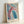 Soft abstract floral artwork with layered pink and blue petals, evoking a meditative, intimate aesthetic on the wall.