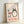 Studio Ghibli-inspired poster showing Totoro and umbrella-holding child at a bus stop in gentle rain, combining minimalist linework with warm cream, charcoal, and coral red color scheme.