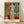 Framed modern art print of a contemplative woman with hands behind her back, rendered in ochre, brown, and cream tones with muted green accents in an Art Nouveau style.