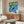 Folk art-inspired wall print depicting a tranquil scene of an otter in water with surrounding vegetation in muted cream, forest green, and deep blue tones.