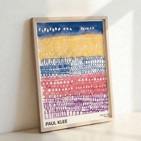 Framed Bauhaus artwork depicting stylized city buildings with geometric shapes in soft palette of purple, gold, and blue hues.