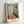 Serene abstract poster art in cream and soft pastels showing a contemplative woman near a window, rendered in minimalist cut-out style with an elegant, peaceful atmosphere.