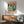 Midcentury modern wall art depicting a piano keyboard transitioning into a city skyline with musical notes scattered throughout, painted in retro palette of coral, mustard, and forest green.