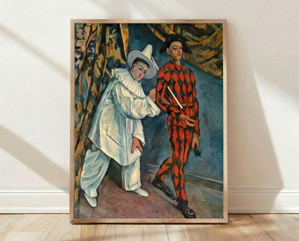 Framed poster of Cezanne's Pierrot and Harlequin, depicting two costumed figures in muted earth tones and soft blues against an abstracted background, hanging on a wall.