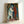 Vintage-inspired framed artwork showing two theatrical characters in Pierrot and Harlequin costumes, painted in subdued palette of cream, rust, and slate blue.