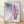 Soft watercolor painting of a pink banana flower with layered petals in rose and lavender tones, surrounded by sage green leaves in a serene botanical composition.