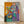 Abstract Matisse-style framed poster featuring a figure in a purple robe surrounded by vibrant anemone flowers in bold, expressive colors on a wall.