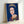 Framed pop art poster of Queen Elizabeth II rendered in deep blue with simplified, geometric facial planes and bright accent colors, modern wall art.