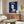 Dark blue pop art interpretation of Queen Elizabeth II with simplified contours and vivid color accents, Reigning Queens series aesthetic on gallery wall.