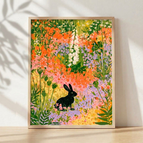 Whimsical boho art print featuring a black rabbit surrounded by vibrant wildflowers in orange, pink, and lavender tones set in a serene meadow, framed on a wall.