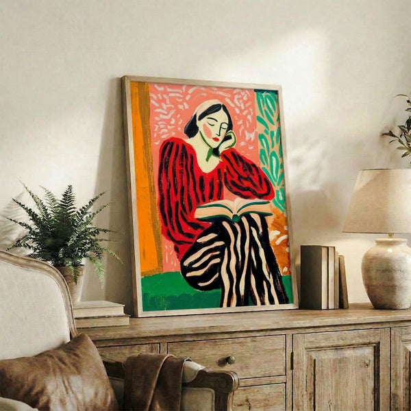 Vibrant pop art wall print of a woman absorbed in reading, dressed in a red striped sweater and surrounded by stylized green foliage, executed in bold black lines and warm coral and orange hues.