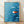 Minimalist Japandi poster featuring a solitary orange-red koi fish swimming upstream against a serene cerulean and teal gradient background, framed on a wall.