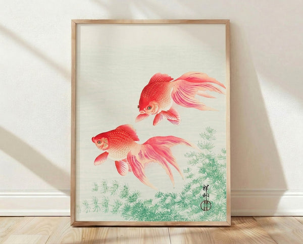 Framed Japanese woodblock print of two goldfish swimming among aquatic plants in soft coral red and sage green tones, evoking serene natural beauty.