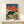 Vintage-style woodblock art print showing a wild bear standing in an ochre grassland with dramatic crimson peaks and dark navy sky, evoking traditional Japanese mountain landscape aesthetics.