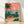 Retro-style coastal art print featuring a bicycle leaning against a palm tree on a beach at golden sunset, rendered in warm coral, sage green, and teal tones.