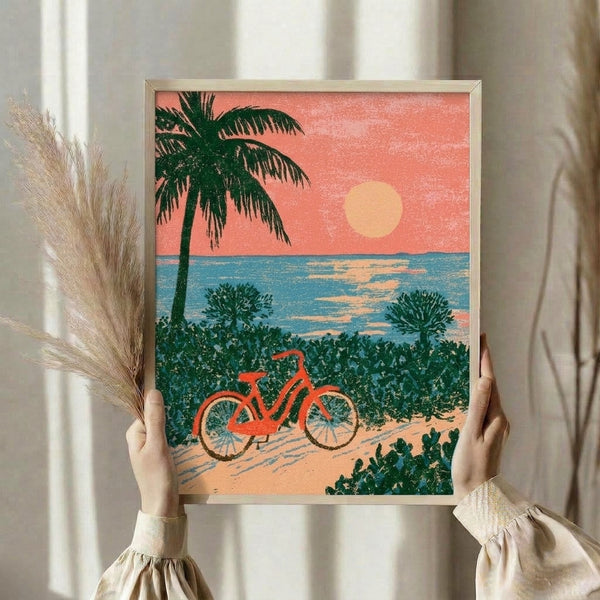 Framed retro coastal artwork depicting a relaxing beach landscape with bicycle, palm tree, and vibrant sunset in warm coral and cream hues.