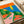 Mid-century modern art print depicting a nostalgic road trip scene with a vintage automobile, coastal cliffs, blooming flowers, and a vibrant sunset in blue, orange, and green tones.