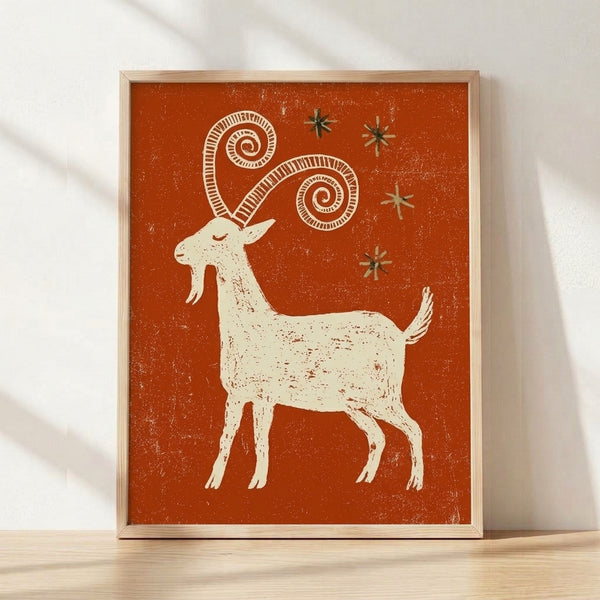 Whimsical folk art poster featuring a rust orange goat surrounded by stars and spiral motifs in cream, olive green, and burnt sienna tones, framed on a wall.