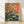 Retro-style framed poster art featuring a praying mantis perched among wildflowers and grasses in warm rust orange, sage green, and navy blue tones against a cream background.