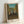 Framed print of The Football Players by Henri Rousseau, showcasing figures at play in a dreamlike woodland setting with cream, teal, and ochre palette in his distinctive folk art style.