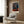 Distorted figurative study in grey, brown, and black tones showing a seated form on furniture, radiating existential unease through fragmented, abstract treatment.