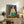 Abstract-influenced portrait of a seated figure in flowing dress, set against layered patterned designs in warm and cool colors, presented as a gallery-quality poster.