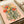 Poetic dark botanical poster depicting a skeleton ribcage transformed into a floral arrangement with whimsical pink and coral flowers, golden accents, and sage foliage, celebrating life and mortality.