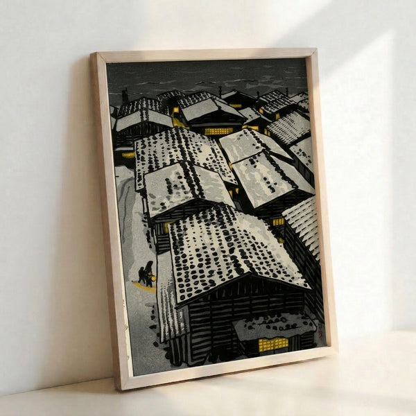 Vintage Japanese-style woodblock poster featuring snow-laden rooftops and buildings rendered in charcoal black, cream white, and soft gold accents, with lanterns punctuating the serene night scene.