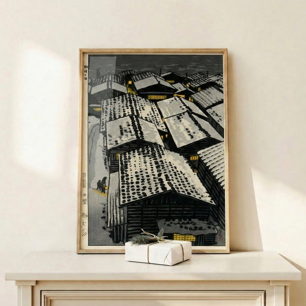 Framed woodblock print of a snowy village with detailed rooflines, glowing lanterns, and a contemplative figure, combining traditional Japanese art style with muted grey and warm golden tones.