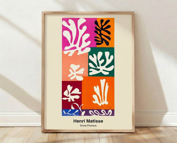 Abstract floral cut-out art print in vibrant red, blue, and yellow shapes against white, framed on a wall in a minimalist modern style.