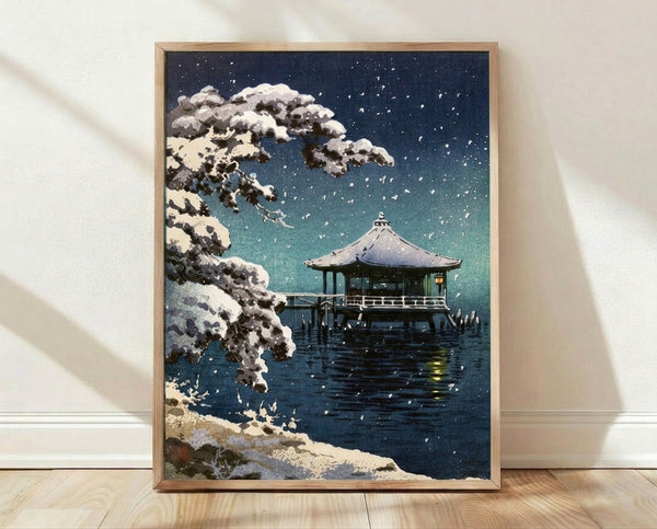 Serene Japanese woodblock print featuring a snow-covered pavilion beside calm water under a starlit night sky, rendered in navy, teal, and cream tones.