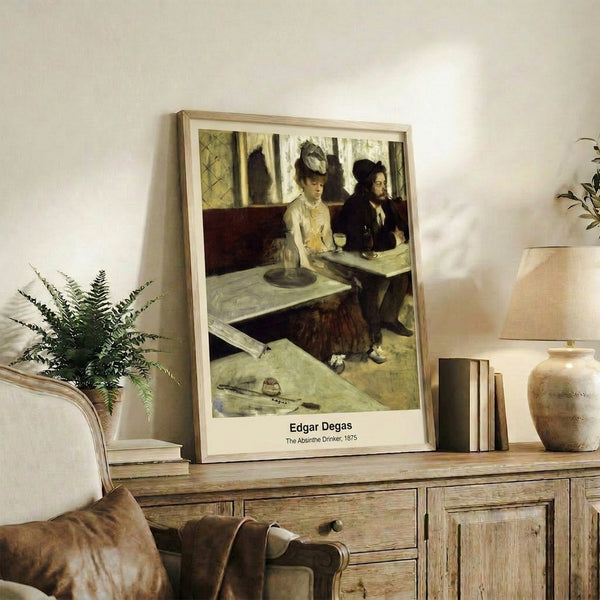 Framed wall art print of a figure at a café table with absinthe, painted in dark browns and cream in an isolated, reflective Impressionist style.