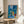 Abstract landscape print framed on wall depicting The Blue Window in muted blues and greens with geometric shapes and a quiet, understated elegance.