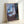 Moody expressionist framed artwork depicting a solitary figure at a window, with atmospheric color palette of soft blues and ochres creating a pensive, introspective atmosphere.