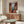 Poster featuring a calm domestic scene rendered in warm beige and soft blue, with abstracted furnishings and window light creating a sense of serene afternoon stillness.