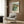 Abstract-modern interpretation of a hillside village with tightly grouped buildings and vegetation in cream, warm brown, and muted green, framed wall art.
