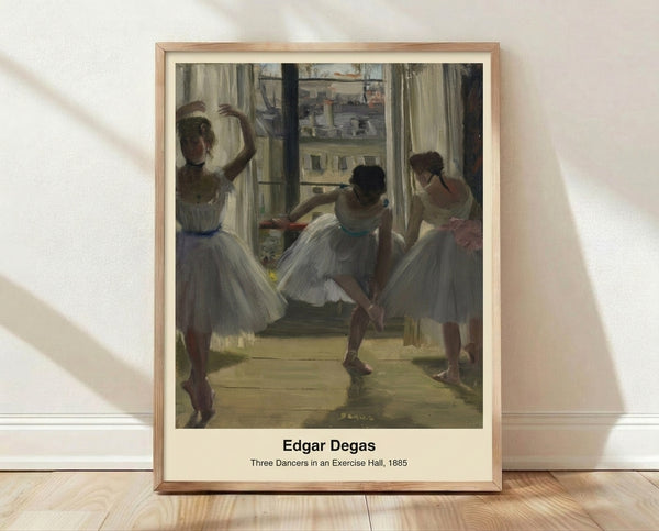 Framed Impressionist artwork depicting three ballet dancers in an exercise hall, rendered in soft cream, ochre, and pale blue tones with an intimate, observational mood.