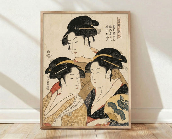 Framed Japanese woodblock print of three elegant geishas in ornate kimonos and traditional hairstyles, rendered in cream, black, gold, and red tones with refined Edo period aesthetics.