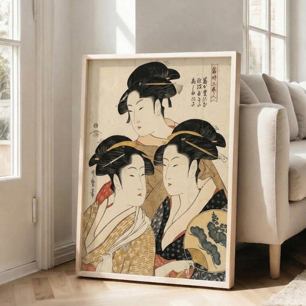 Framed Edo period Japanese art featuring three beautiful geishas holding fans and wearing richly patterned kimonos, rendered in a sophisticated cream, tan, black, and gold palette.