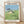 Whimsical Studio Ghibli poster featuring Totoro holding an umbrella in a lush meadow with children among tall grass and flowers in soft blue, green, and cream tones.