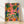 Whimsical boho poster of alligators gathered around a jungle dinner table with tropical fruits, candles, and palm leaves in vibrant coral pink, forest green, and golden yellow tones.