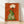 Whimsical folk art poster featuring a turtle cradling a delicate lotus flower in warm rust orange, cream, and forest green tones on a framed wall display.