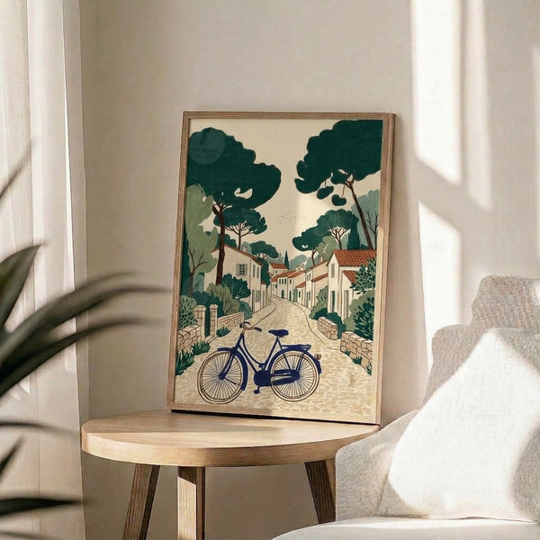 Framed art print depicting an idyllic village lane with a bicycle amid architecture and vegetation, rendered in warm cream, navy, and earthy tones with nostalgic retro charm.