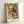 Abstract surrealist artwork depicting two figures alongside a dragonfly in minimalist style using red, blue, yellow, and black elements on a clean white surface.